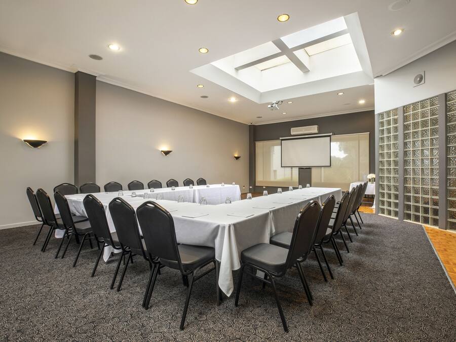 Un salón de conferencias con una larga mesa, sillas, una pantalla de proyector y un amplio ventanal con vistas.