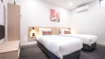 Habitación de hotel con dos camas, un escritorio, aire acondicionado de pared y un cuadro de una flor.