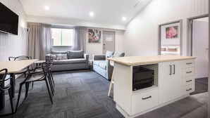 A modern kitchen with a dining area, grey sofas, and a flat-screen TV. - Nightcap at Ferntree Gully Hotel Motel (Ferntree Gully)