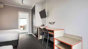 A hotel room with a bed, a desk with chairs, a TV mounted on the wall, and a small window.