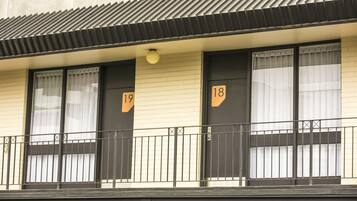 En bygning med nummererede døre, en balkon med gelænder og et tag med fliser.