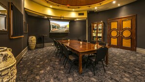 A conference room with a long table, chairs, a projector screen, and a large wooden door. - Nightcap at Matthew Flinders Hotel (Chadstone)
