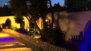 A nighttime view of a building with a stone wall and palm trees. - Millenium Studios (Rhodes)