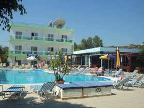 A hotel with a swimming pool, sun loungers, and umbrellas.