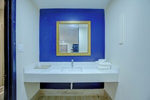 Une salle de bain avec un lavabo blanc, un miroir avec un cadre doré et un mur bleu.