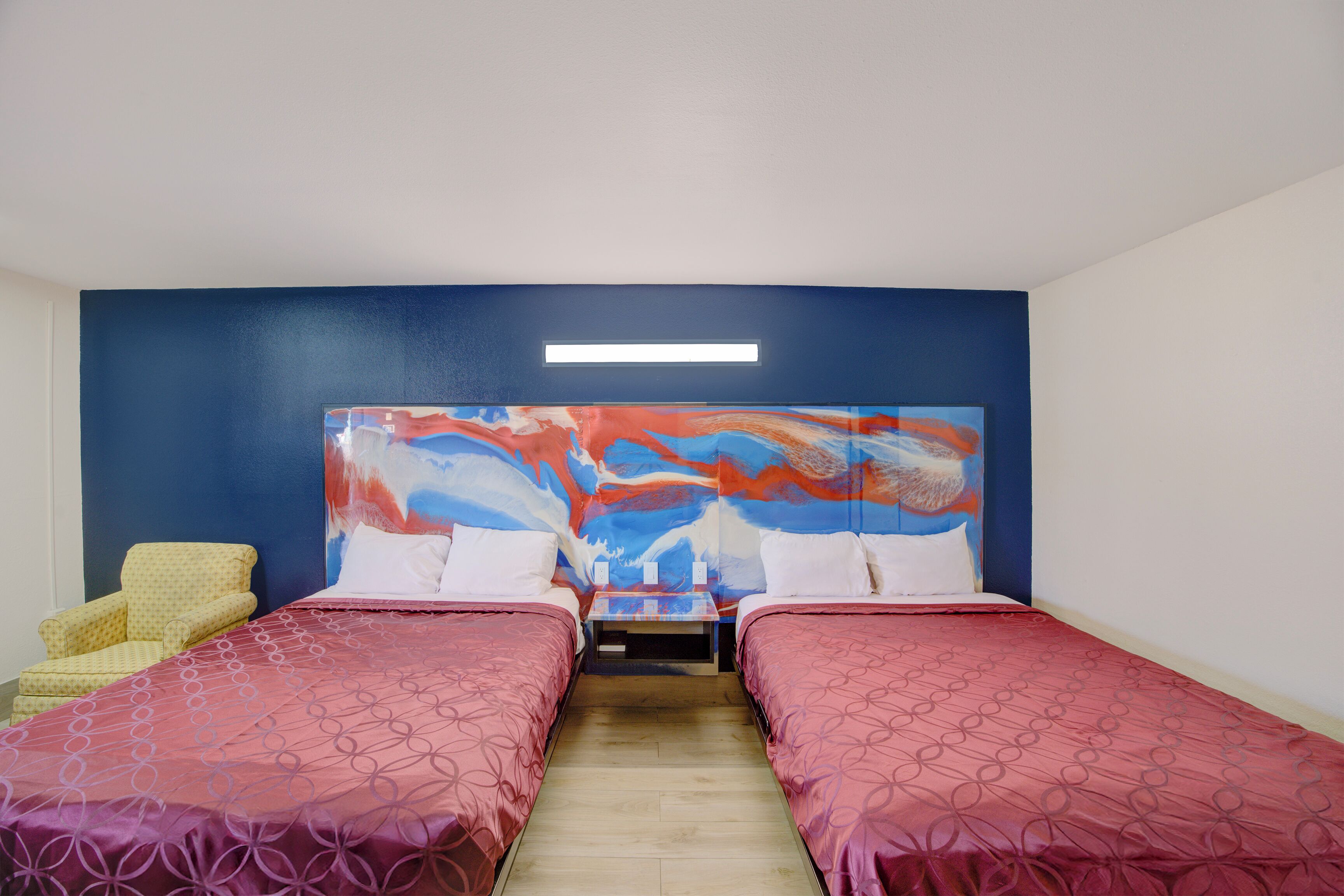 Ein Hotelzimmer mit zwei Betten, einem Nachttisch, einem Sessel und einem großen, abstrakten Gemälde an der Wand.