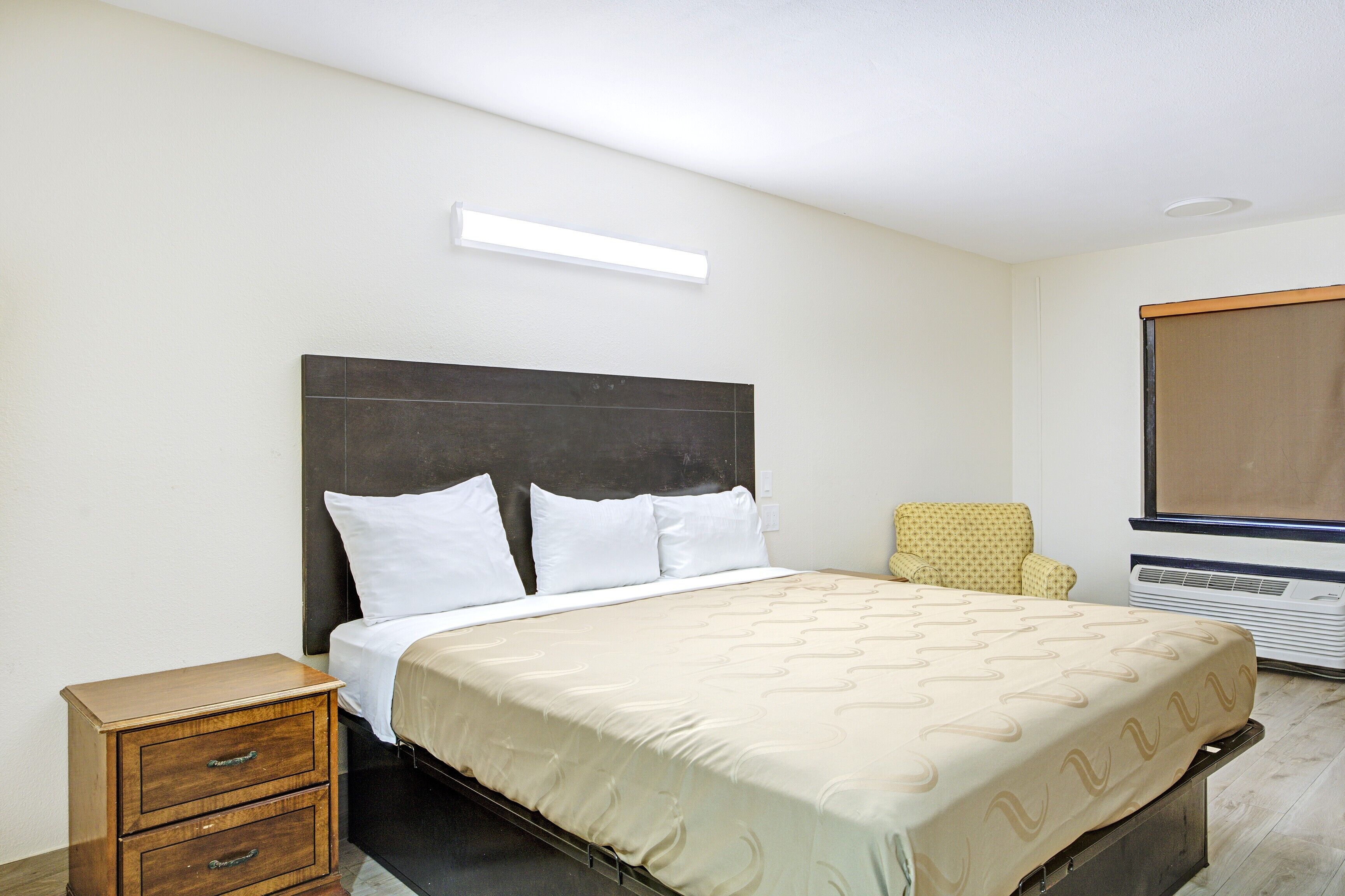 A bedroom with a bed, a nightstand, a chair, and a window.