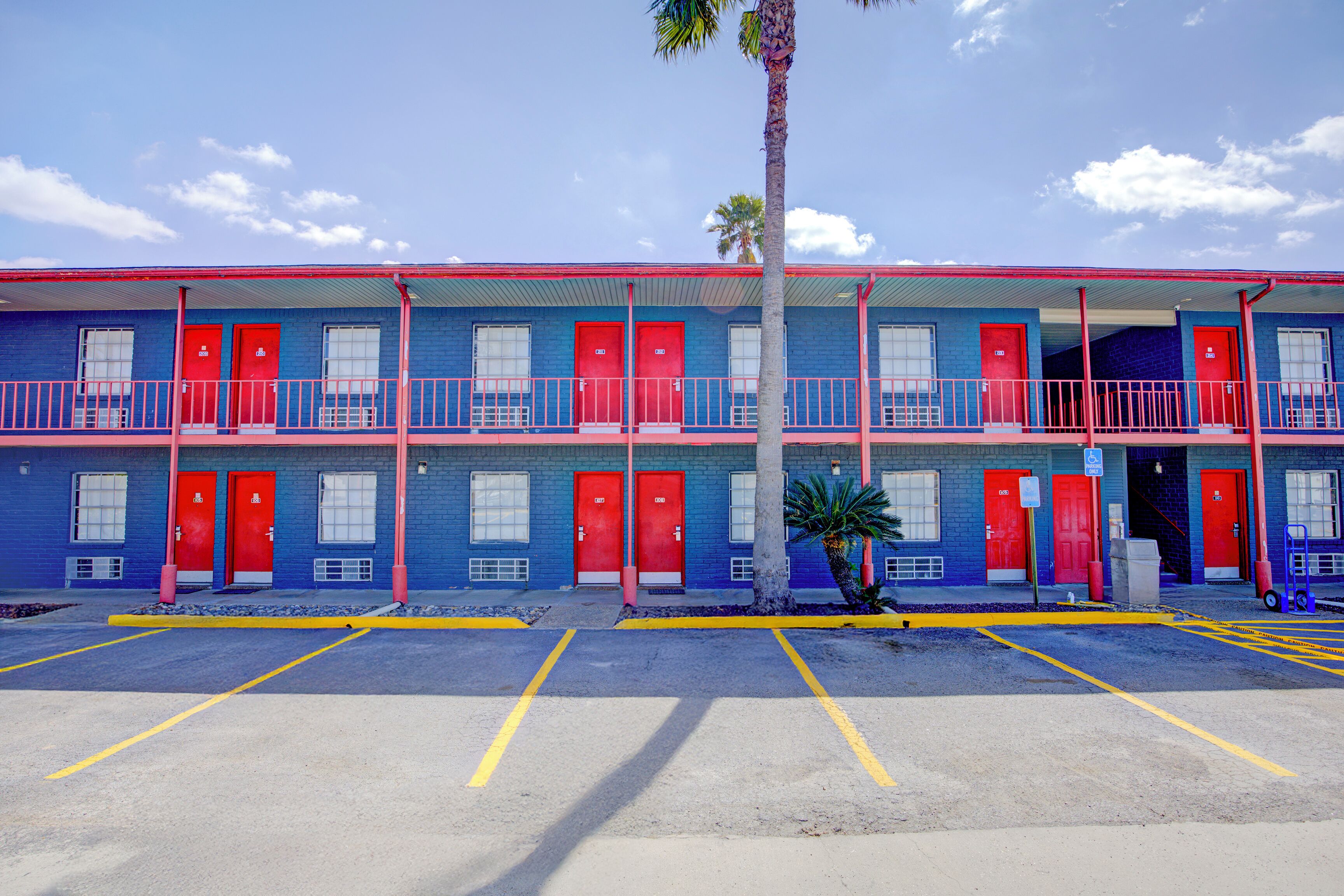 A motel with a two-story structure, red doors, and a parking lot.
