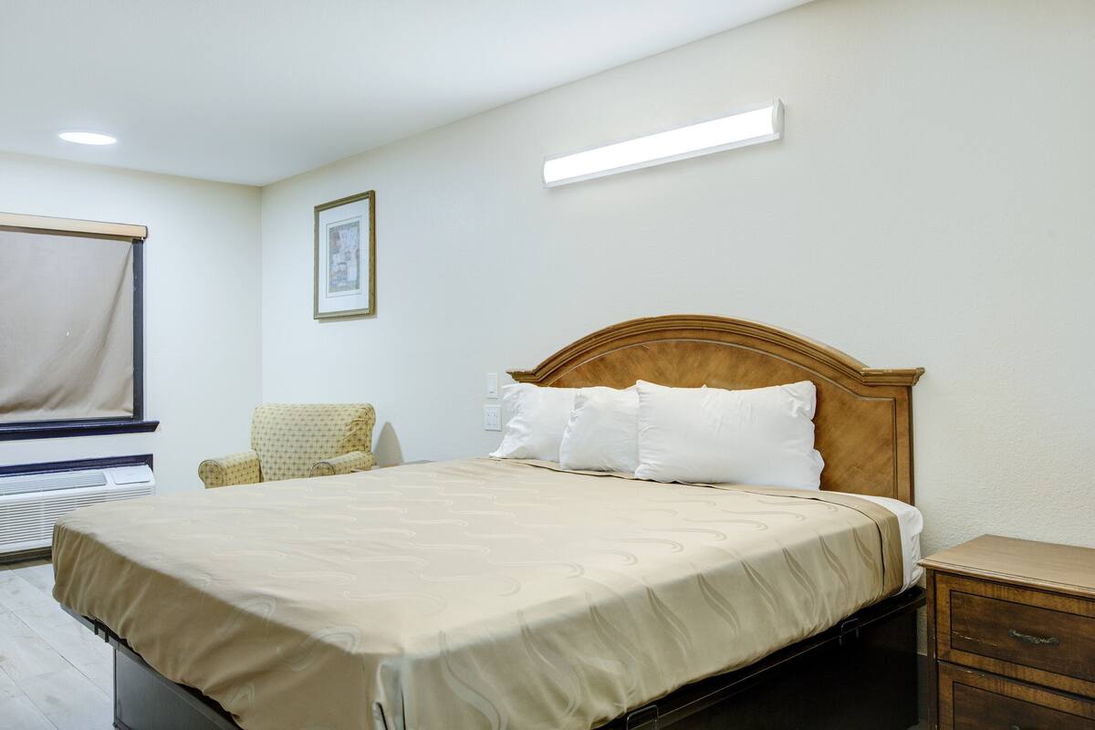 Een keurig opgemaakt hotelkamer met een bed, een stoel, een nachtkastje en een raam met gordijn.