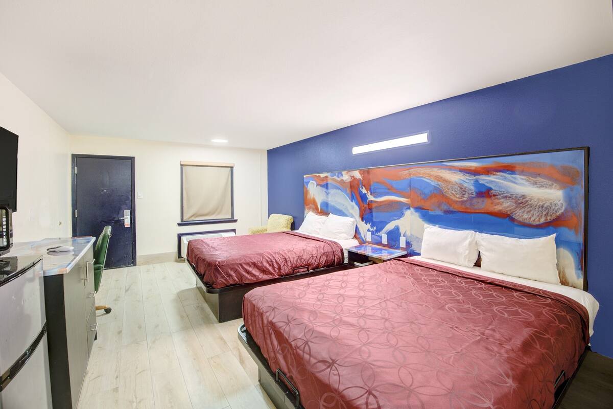 Een hotelkamer met twee bedden, een bureau, een stoel en een groot abstract schilderij aan de muur.