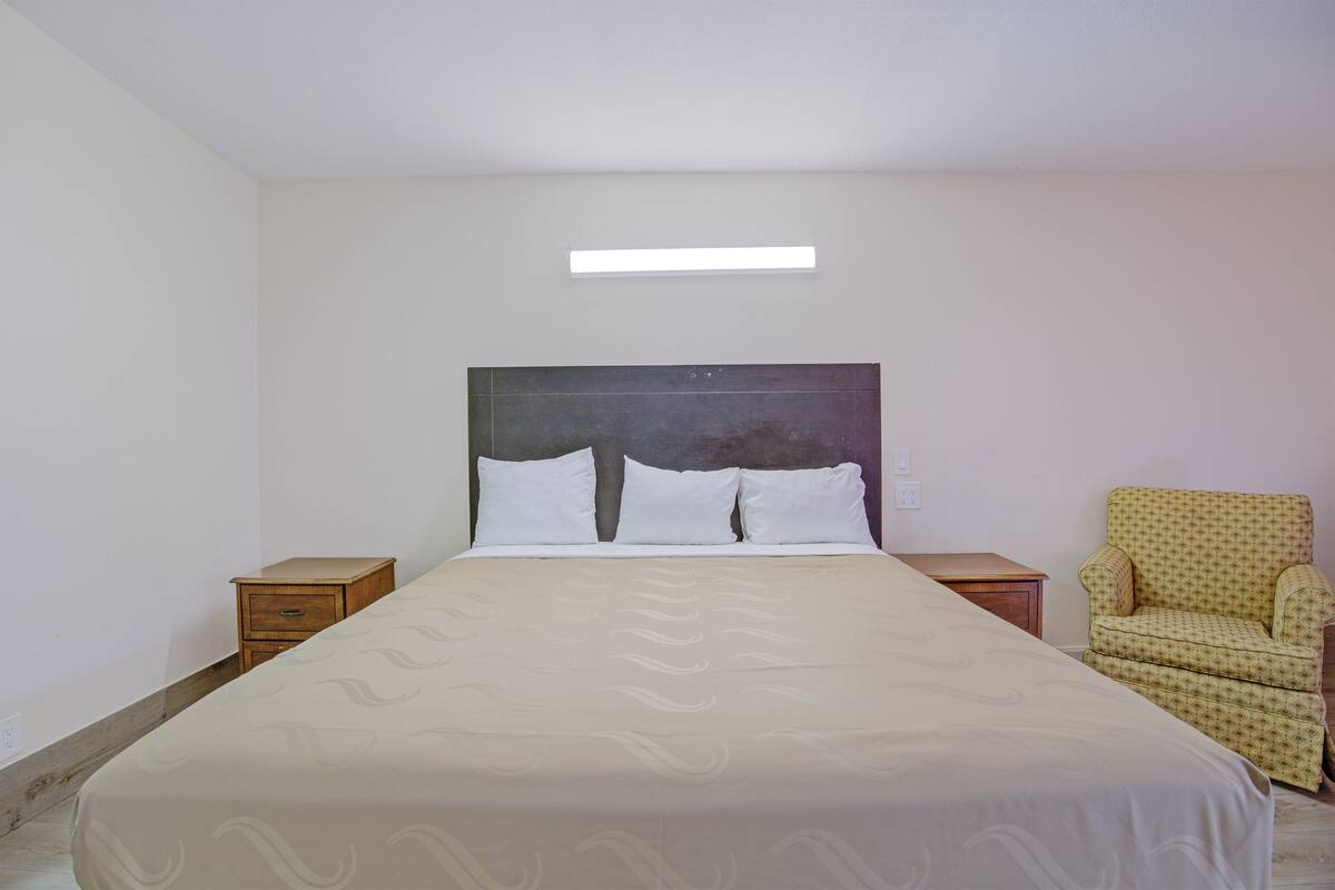 Een slaapkamer met een bed, twee nachtkastjes, een stoel en een hanglamp.