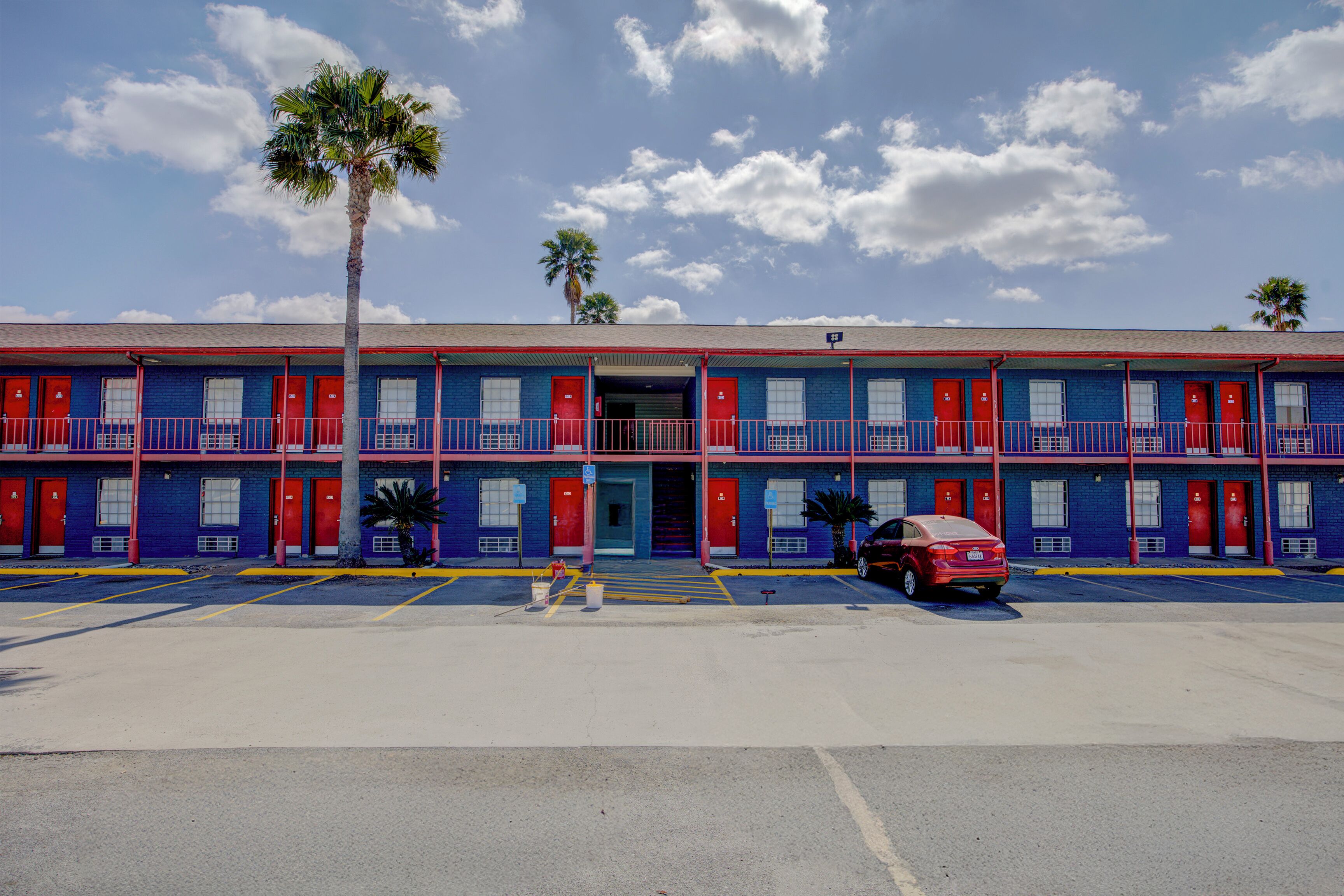 A motel with multiple rooms, a parking lot, and a palm tree.