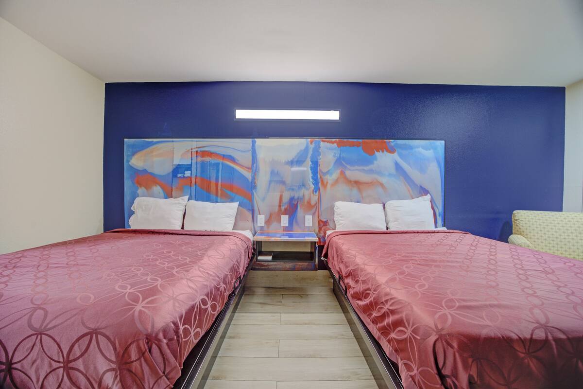 Een hotelkamer met twee bedden, een groot abstract schilderij aan de muur, een nachtkastje en een klein raam.