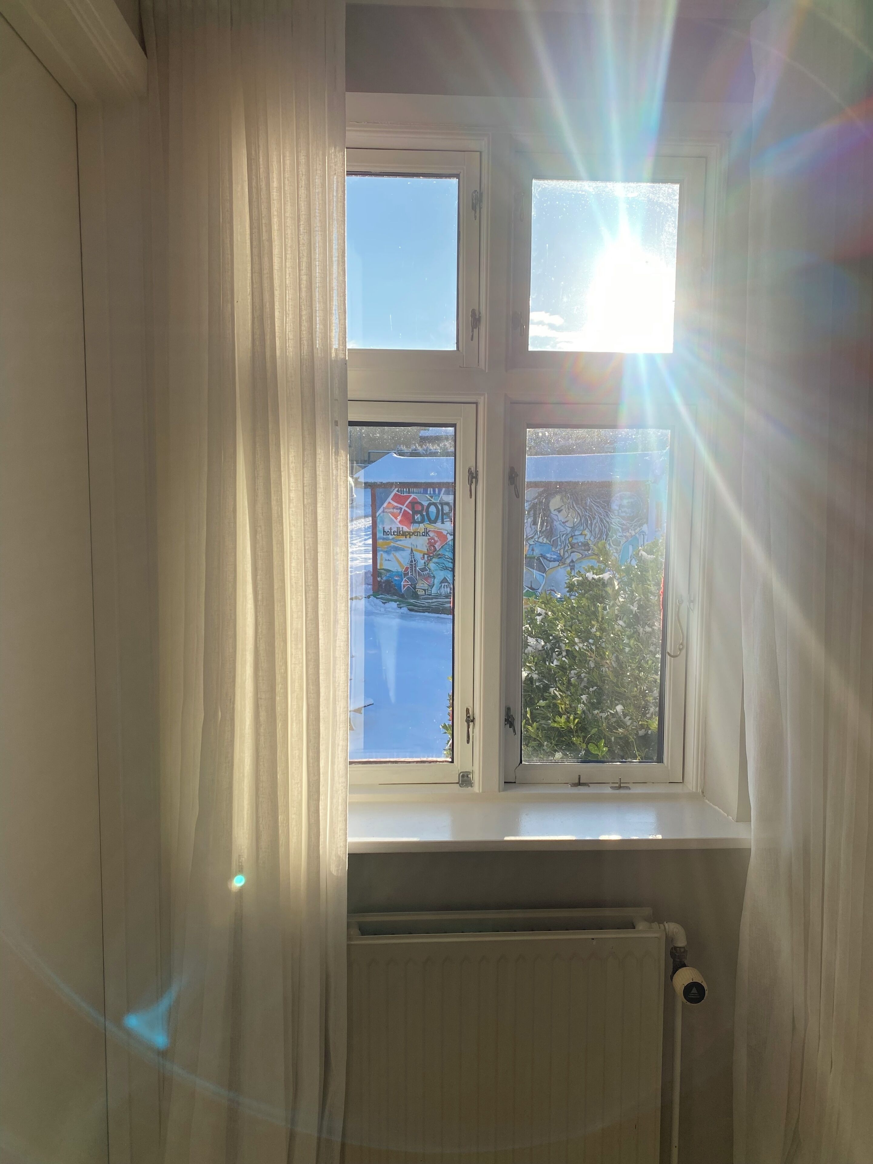 A room with a window overlooking a snowy landscape and a building with a colorful sign.