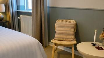 Habitación de hotel con cama, una silla, una mesa redonda con una vela y una ventana con cortinas.