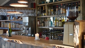 A bar area with shelves of bottles, glasses, and a candle. - Hotel Klippen  (Gudhjem)