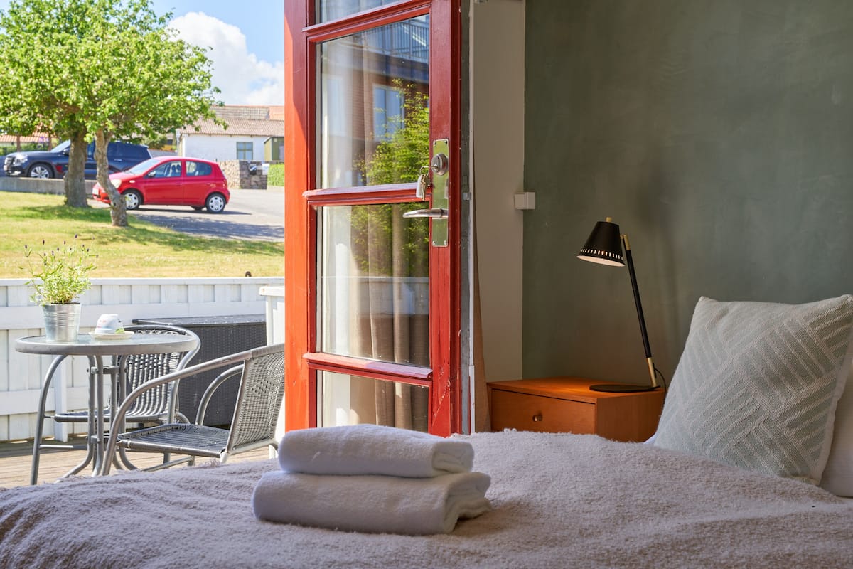 A hotel room with a bed, a nightstand, a lamp, a window, and a view of the outside.