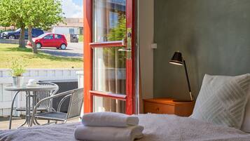 A hotel room with a bed, a nightstand, a lamp, a window, and a view of the outside.