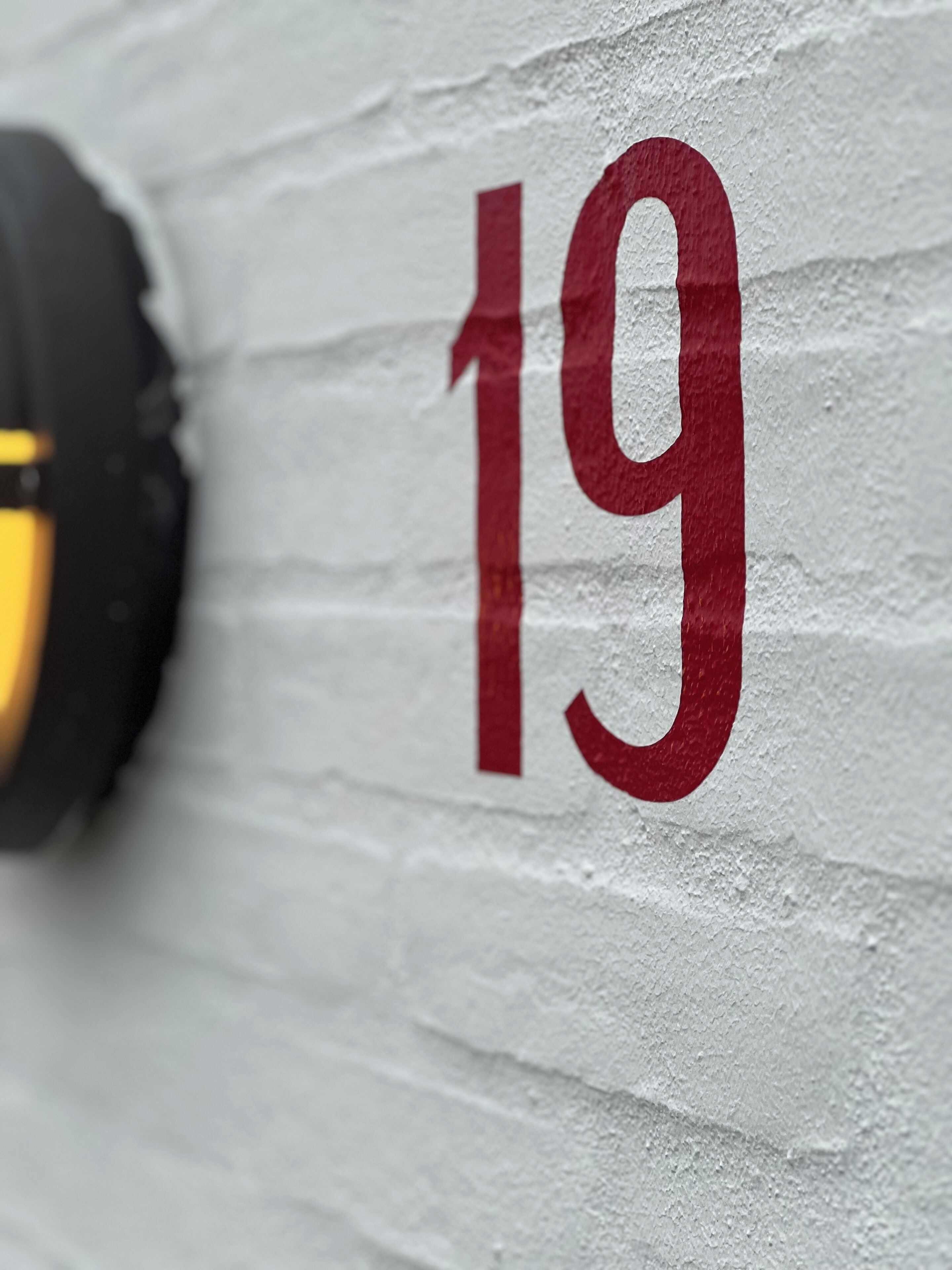 A close-up of a white wall with the number '19' painted in red.