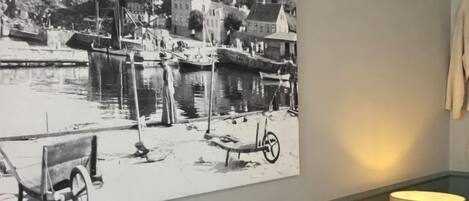 Ein Hotelzimmer mit Bett, Kissen, einer Wandlampe und einem schwarz-weißen Foto einer Wasseransicht.