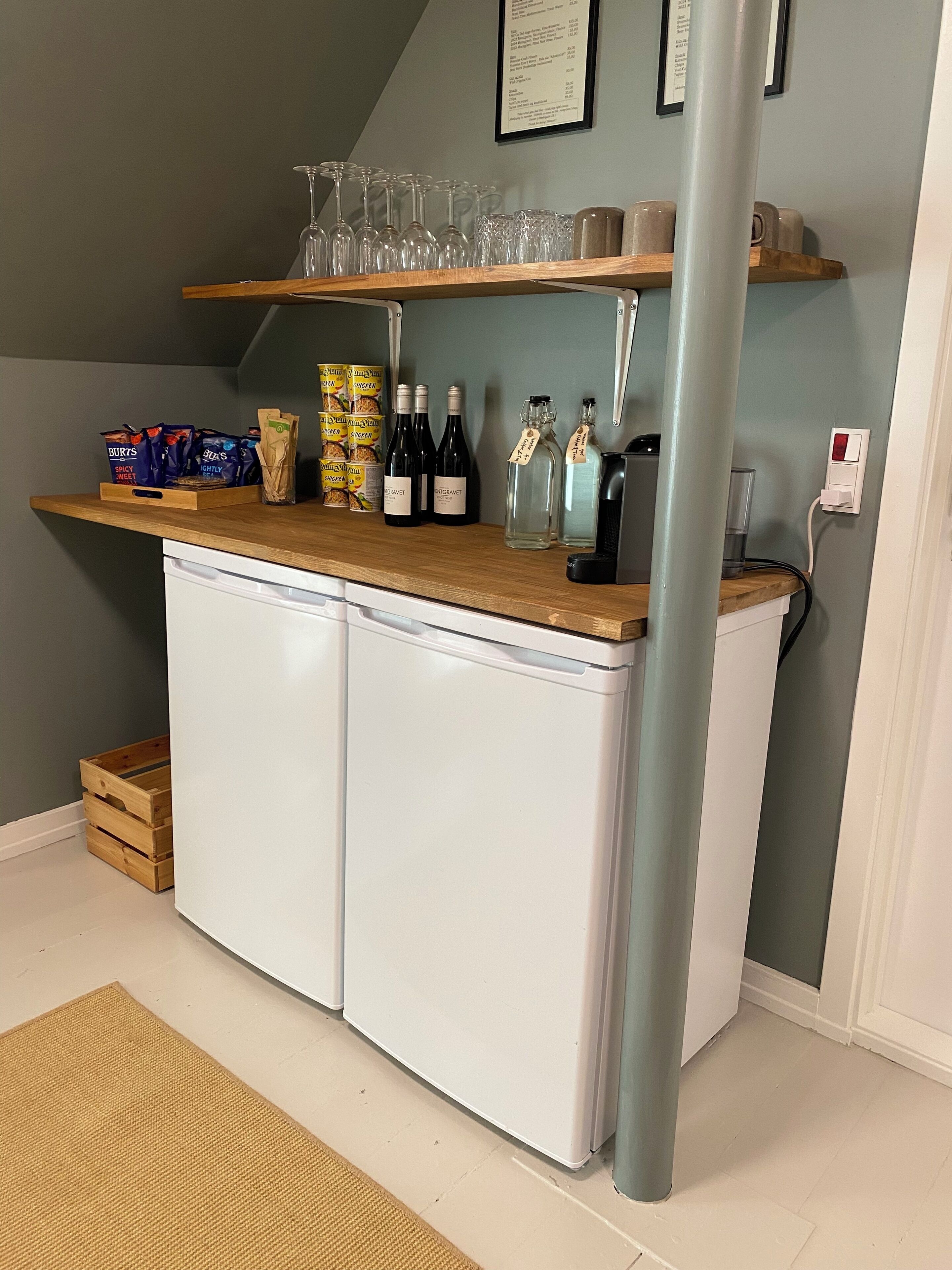 A compact bar area with a wooden countertop, wine bottles, glasses, and packaged snacks.