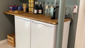 A compact bar area with a wooden countertop, wine bottles, glasses, and packaged snacks.