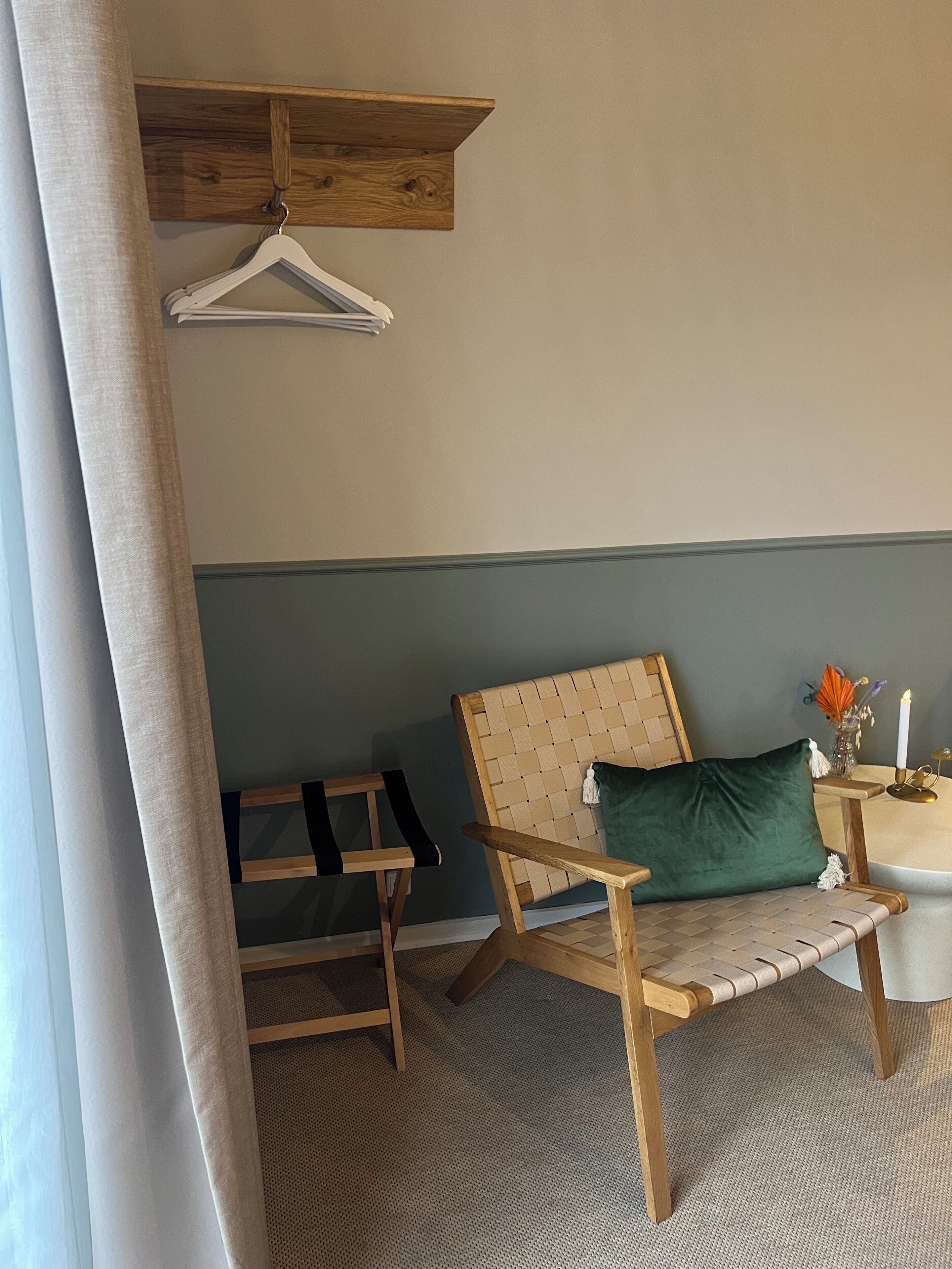 Una habitación con una silla de madera, una mesita con una vela y un perchero.
