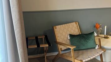 Una habitación con una silla de madera, una mesita con una vela y un perchero.