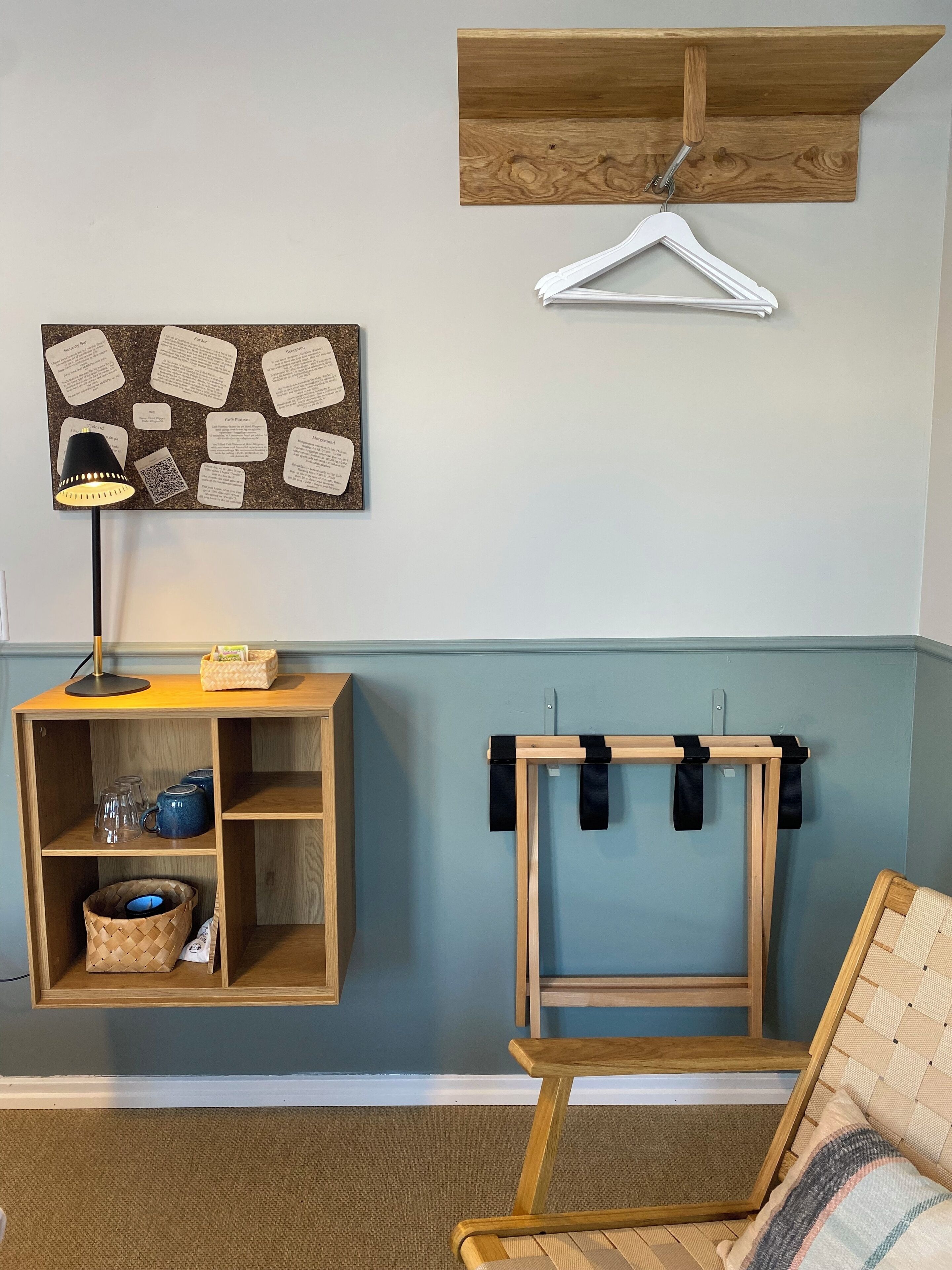 A room with a wooden desk, a hanging light, a corkboard with notes, a wooden shelf, and a chair.