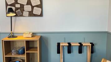 A room with a wooden desk, a hanging light, a corkboard with notes, a wooden shelf, and a chair.