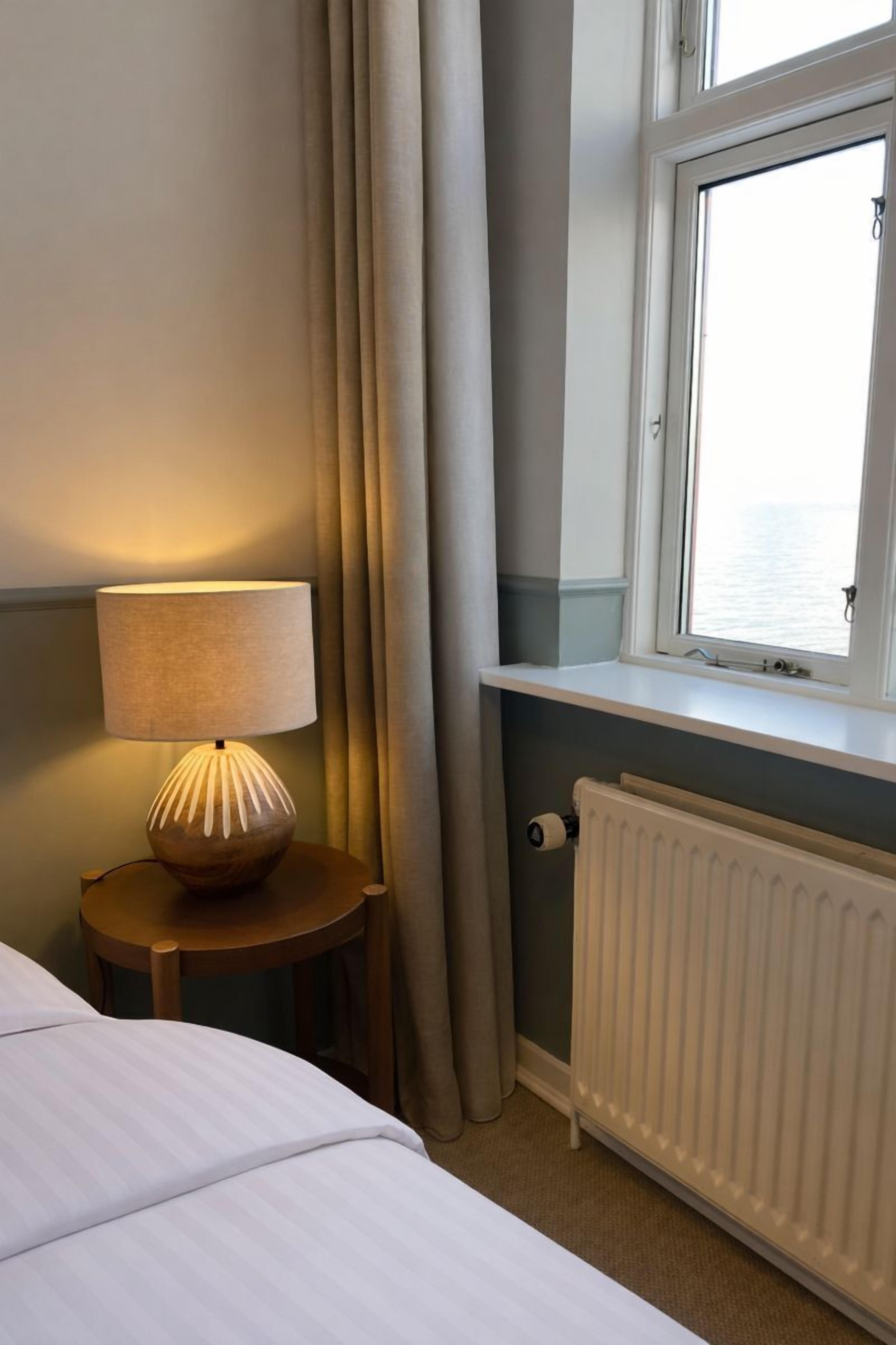 A hotel room with a bed, a bedside lamp, a window with a view, and a radiator.