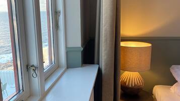 A hotel room with a window, a bedside table with a lamp, and a bed.