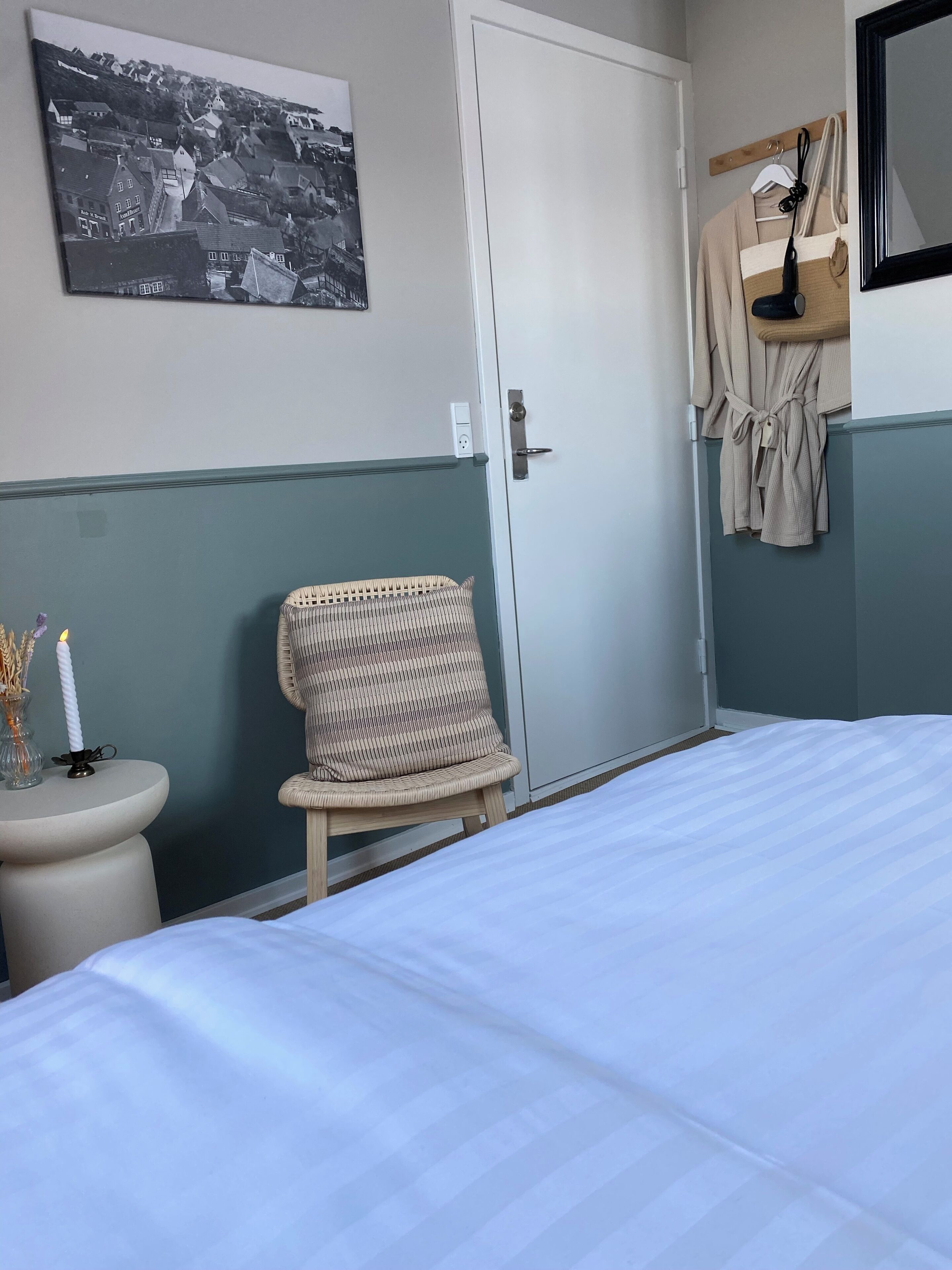 Ein Schlafzimmer mit einem Bett, einem Sessel, einem Nachttisch mit Kerze und einem an der Wand montierten Regal mit einem Bademantel.
