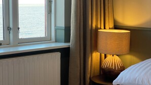 A hotel room with a bed, a window with curtains, and a lamp on a bedside table. - Hotel Klippen  (Gudhjem)