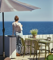 En person står ved et bord med udsigt over havet.