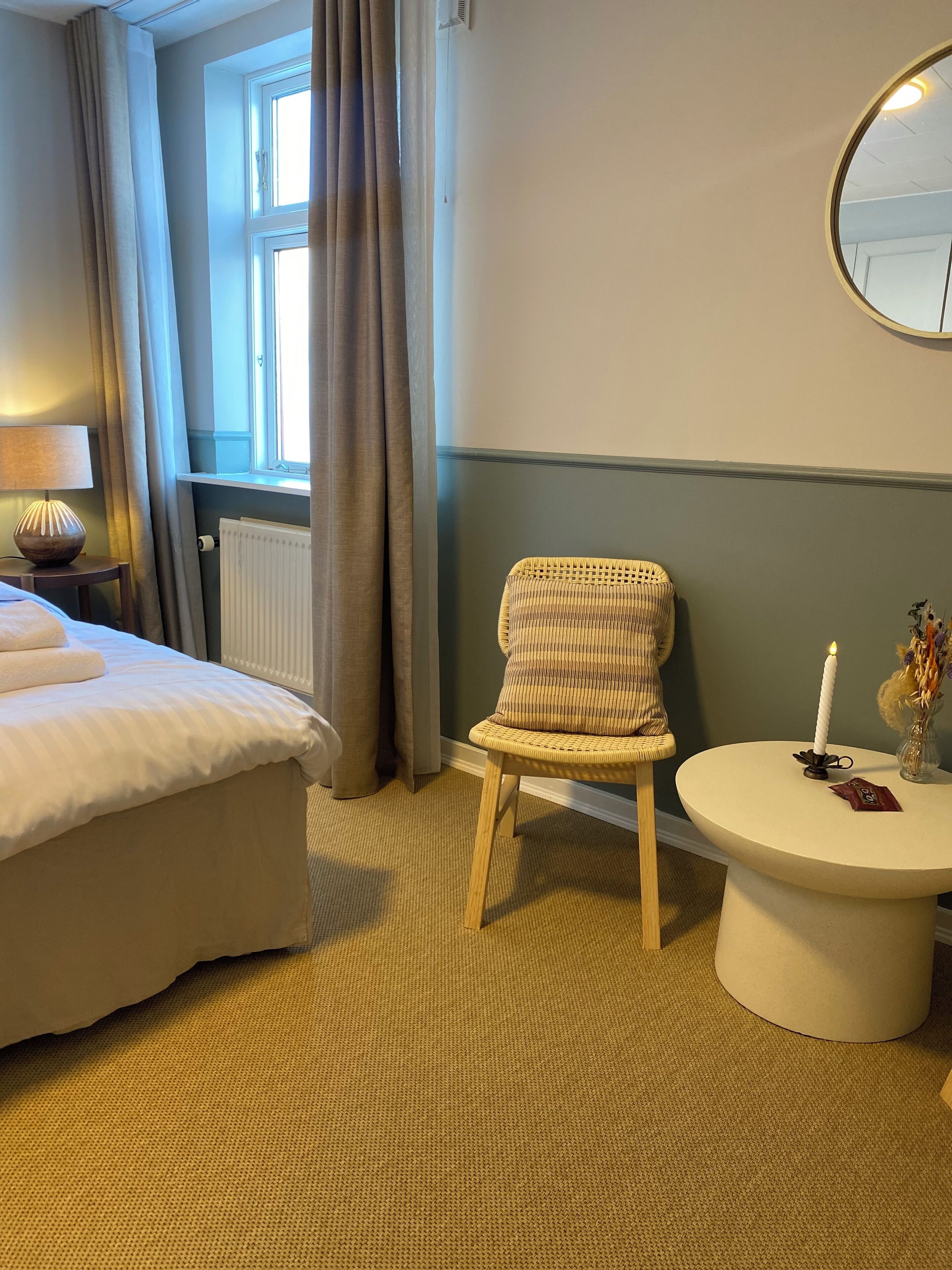 Habitación de hotel con cama, una silla, una mesa redonda con una vela y un espejo en la pared.
