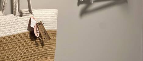 Quarto com prateleira de madeira sobre uma parede branca, exibindo cabides brancos e uma bolsa trançada com etiqueta.