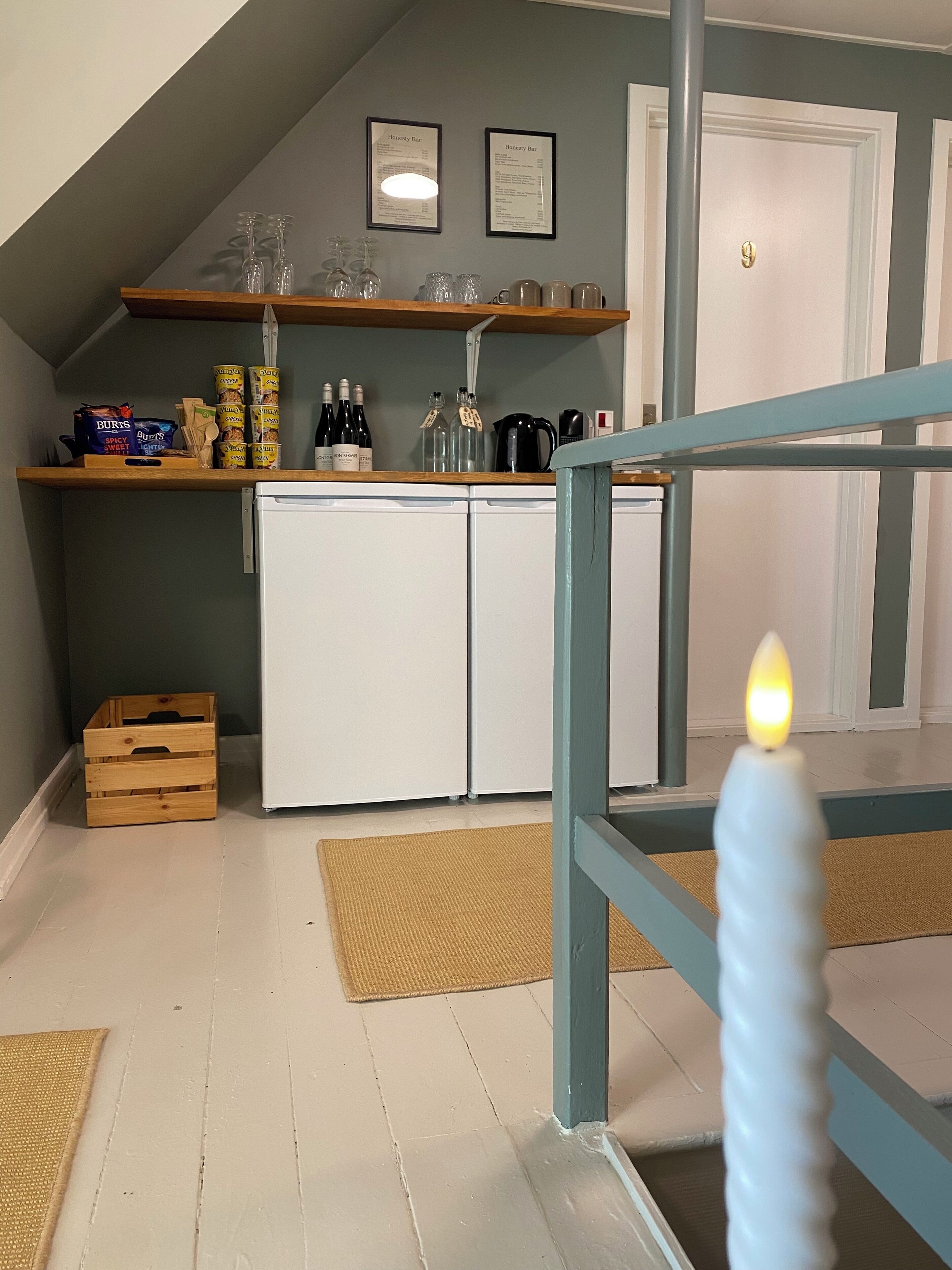 Una cocina con un refrigerador blanco, un estante de madera con cristalería y una puerta con pomo dorado.