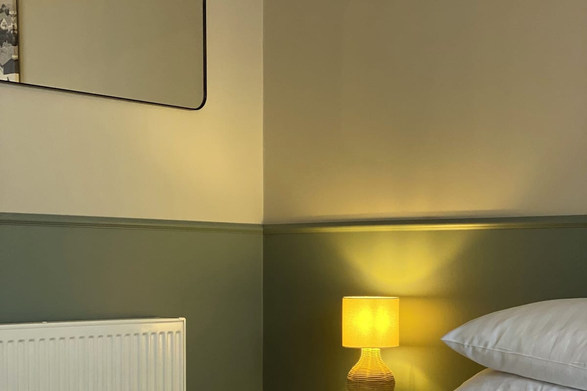A neatly made bed with white linens and two rolled towels, a bedside lamp, and a wall-mounted picture frame.