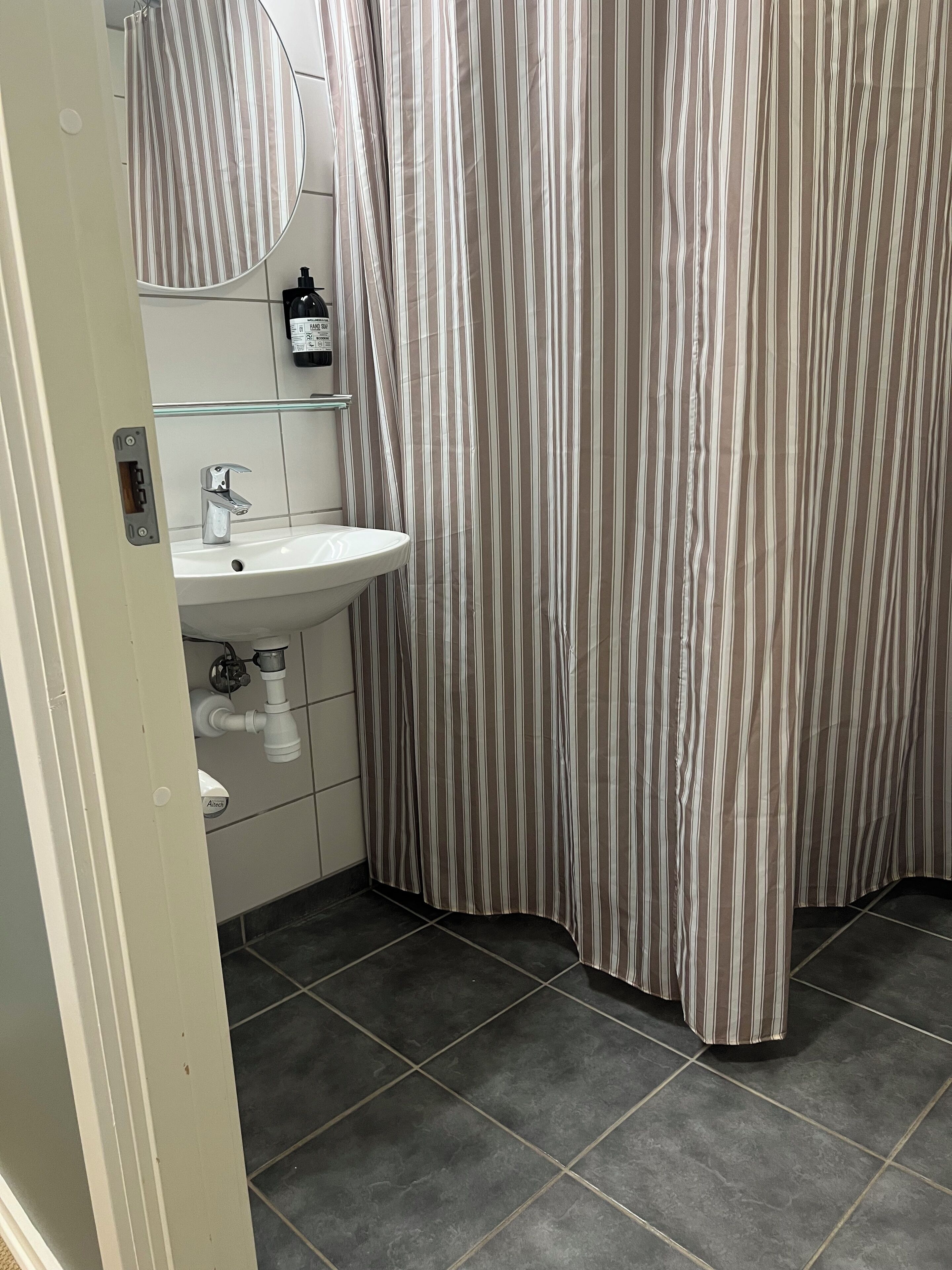 Un baño con un lavabo blanco, un espejo y una cortina de ducha a rayas.