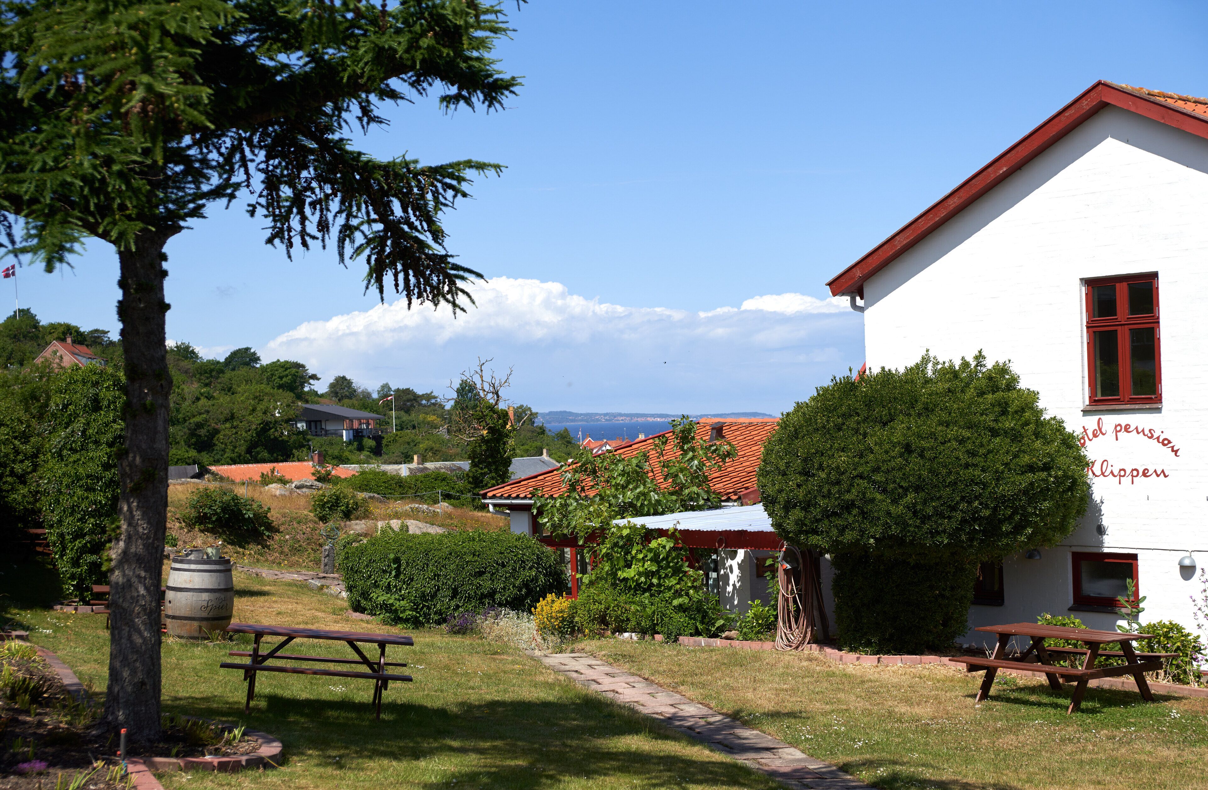 A white building with a red roof, a picnic table, and a barrel in a garden setting.