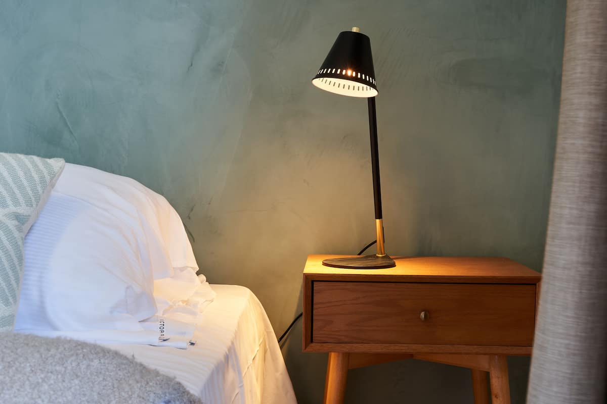 A bedroom with a bed, a bedside table with a lamp, and a wooden nightstand.