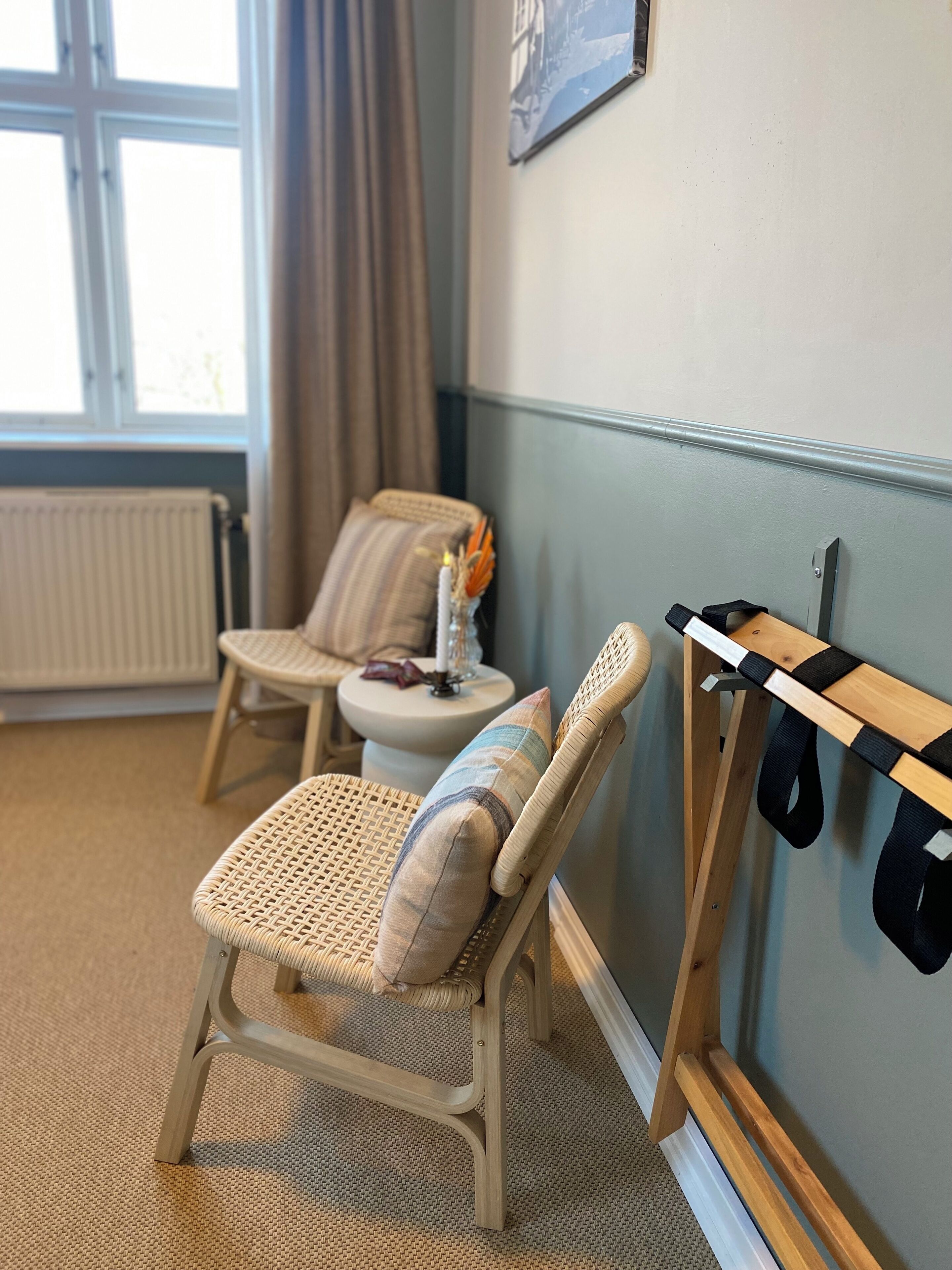 A room with a wicker chair, a small table with a candle, and a coat rack.