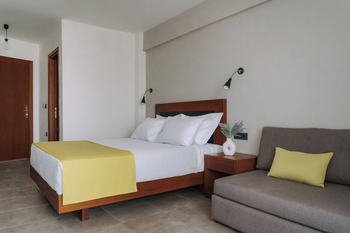 A neatly arranged bedroom with a bed, bedside table, lamp, and a sofa.