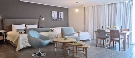 A modern hotel room with a bed, a sofa, a dining table, and chairs.