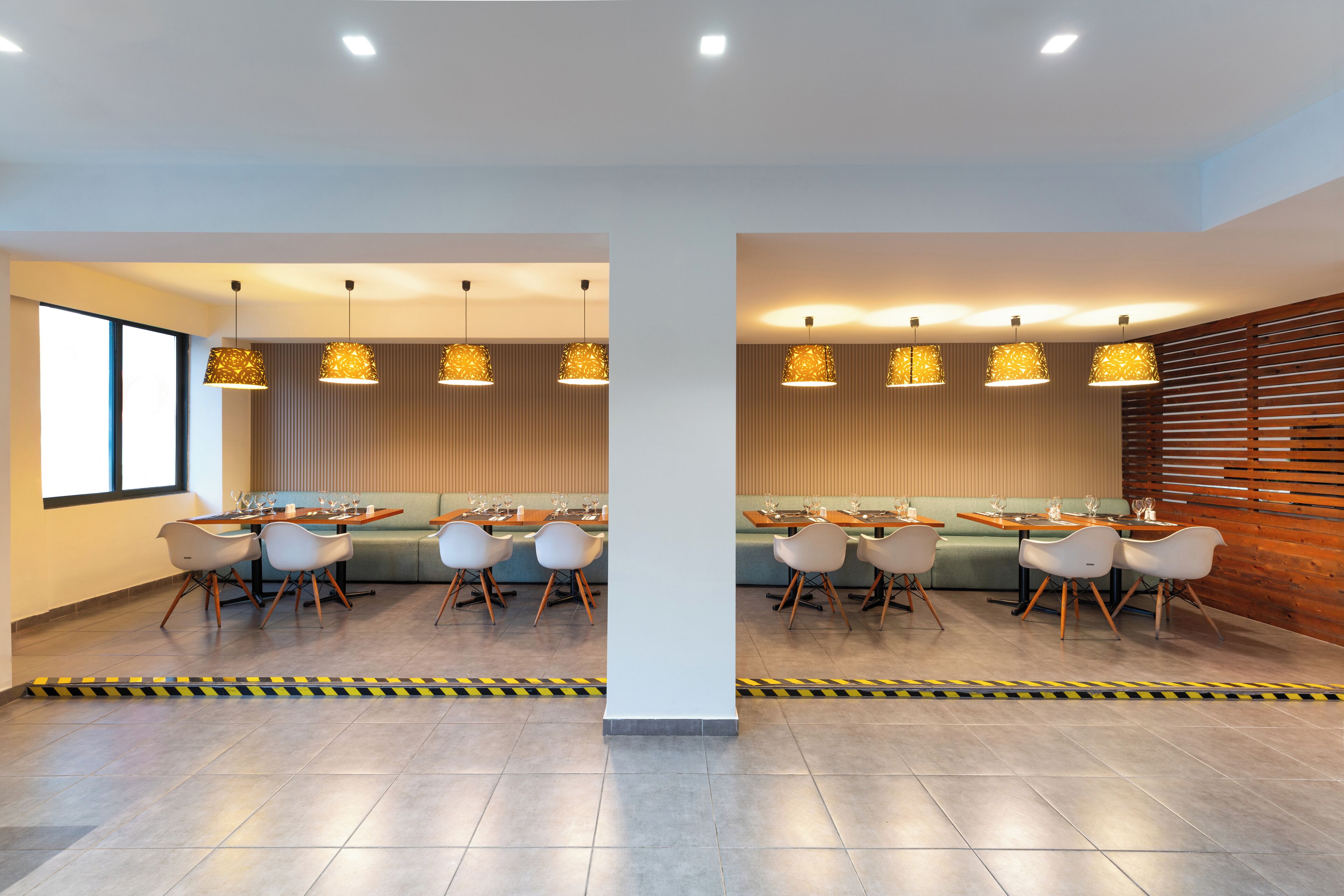 A modern dining area with two long tables, white chairs, and pendant lighting.