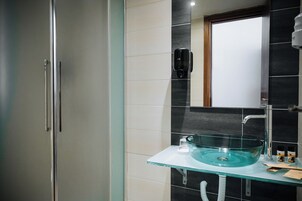 Une salle de bain avec un lavabo en verre, un miroir, une douchette à main et des toilettes.
