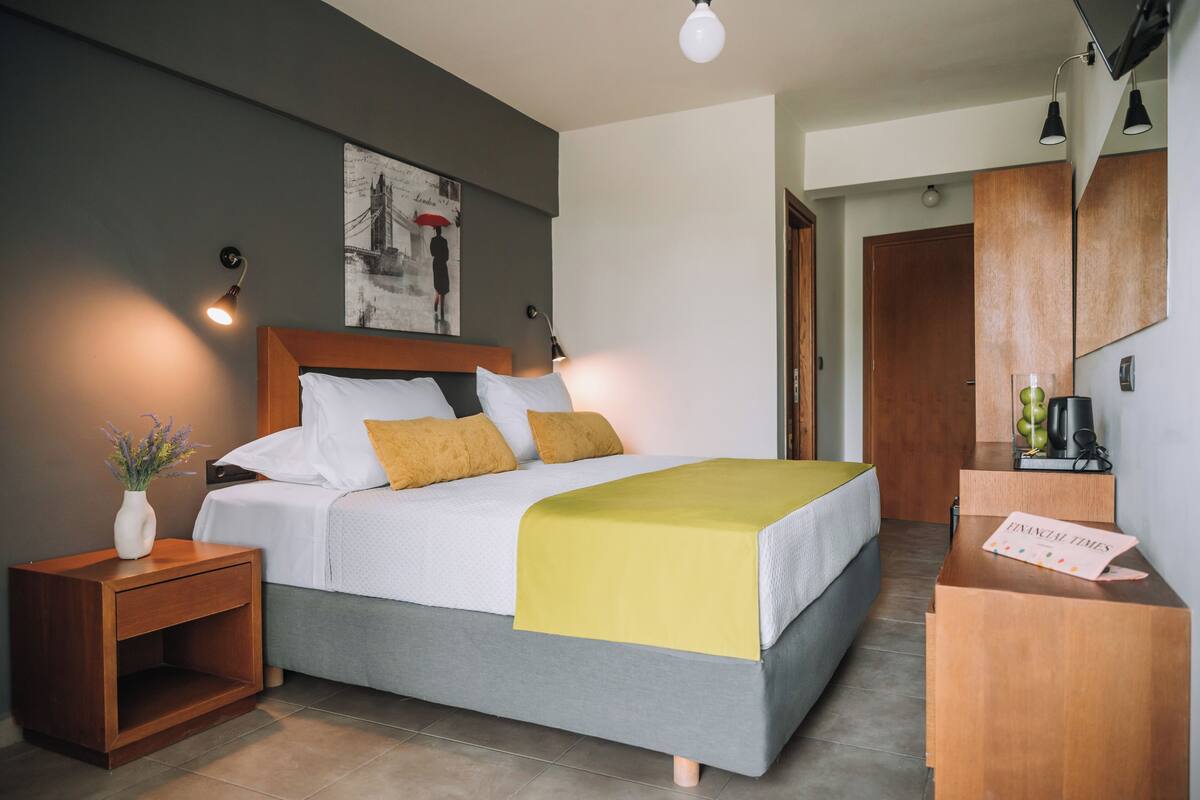 A modern hotel room with a bed, bedside table, and a desk with a mirror.
