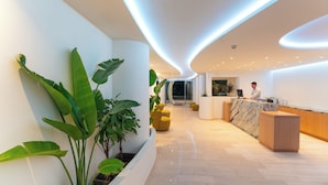A modern reception area with a curved ceiling, a marble counter, and potted plants. - Amphitryon City Hotel (Rhodes)