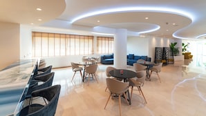 A modern hotel lobby with a long dining table, several round tables, and comfortable seating areas. - Amphitryon City Hotel (Rhodes)